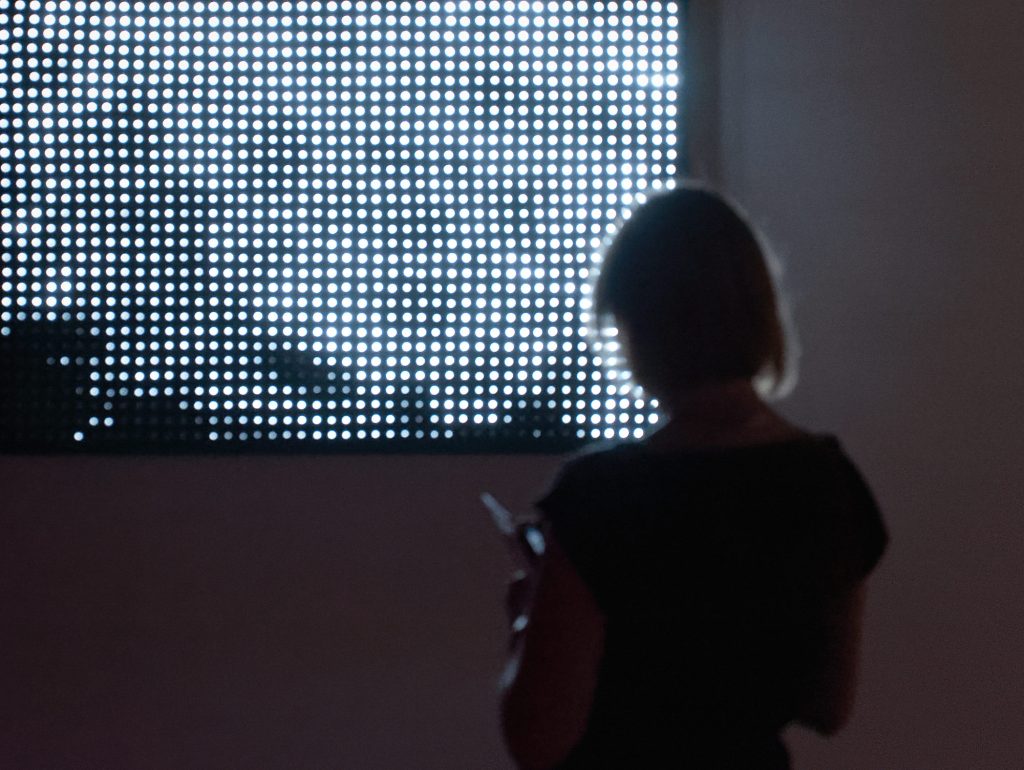 Mujer observando una instalación lumínica de Jim Campbell en una sala de exposición.
