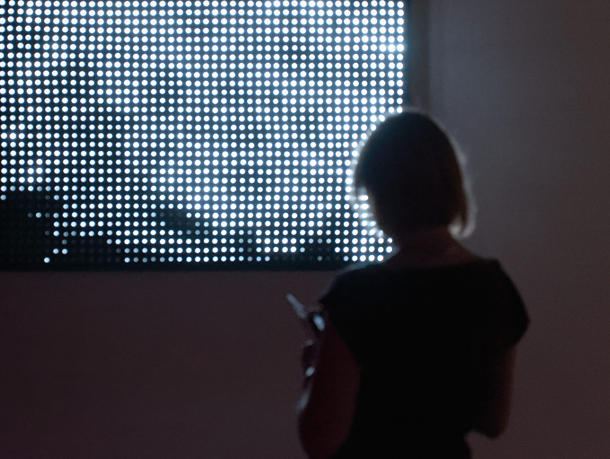 Mujer observando una instalación lumínica de Jim Campbell en una sala de exposición.