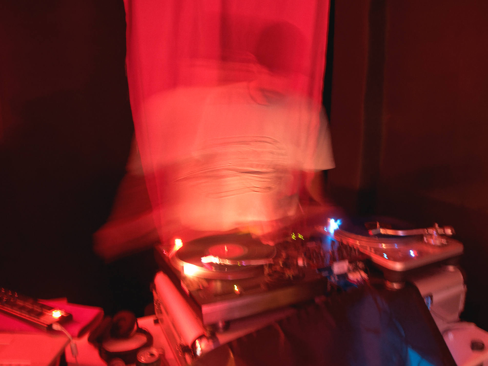 Historia de la Música Electrónica en España: DJ en cabina con dos platos y mesa de mezclas, luces rojas y azules; fotografía de Luis Miguel Fernández.